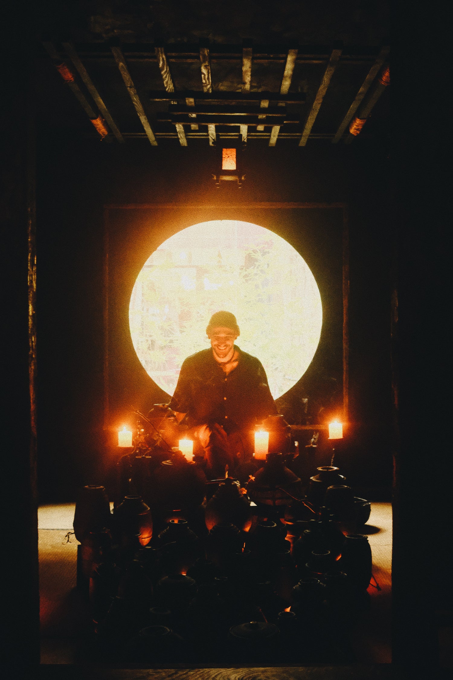 Person standing in front of a large illuminated circle with candles around, in a dark setting.